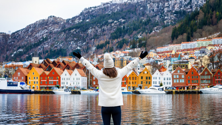 A happy tourist woman enjoys the beautiful view of the Bryggen district in Bergen, Norway, during a cold winter day with snow