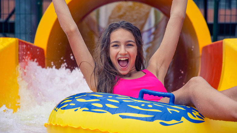 A smiling girl in an inner tube with her arms raised after coming down a waterslide