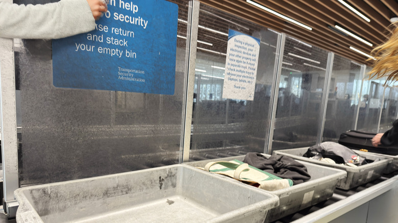 Row of plastic bins on a conveyor belt passing through airport security.