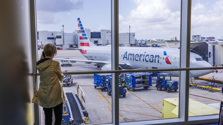 Passenger at gate looks out the window at American Airlines plane on tarmac at Miami Airport.