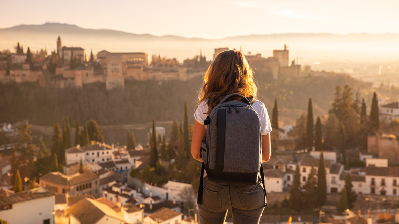 Traveler standing at a viewpoint looking down on a city during sunset