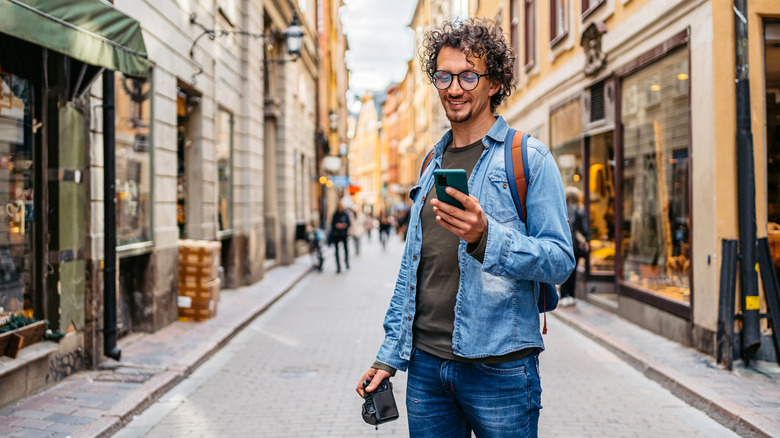 Traveler in Europe checking his phone and holding a camera