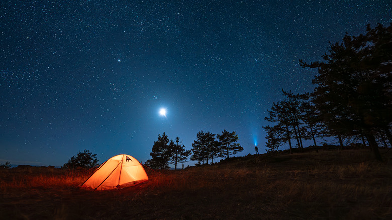 a tent at night illuminated from inside with sky full of moon and stars in background