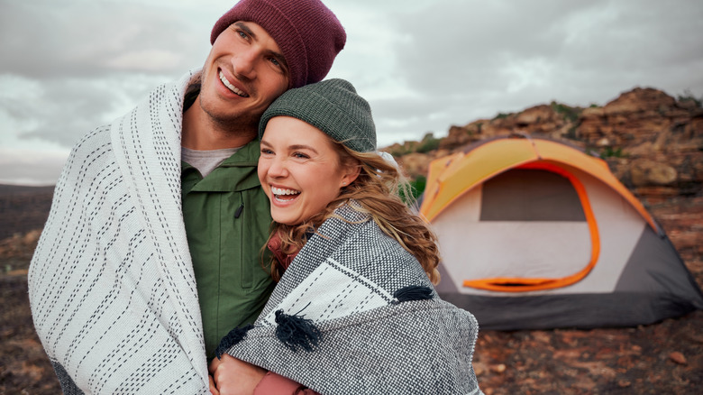 a man and woman wrapped in a blanket outside their tent