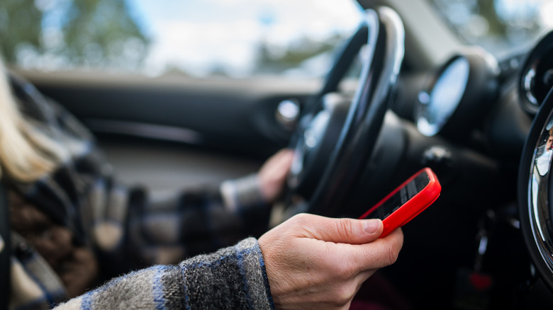 Close up of driver with one hand on the wheel and cellphone in the other.