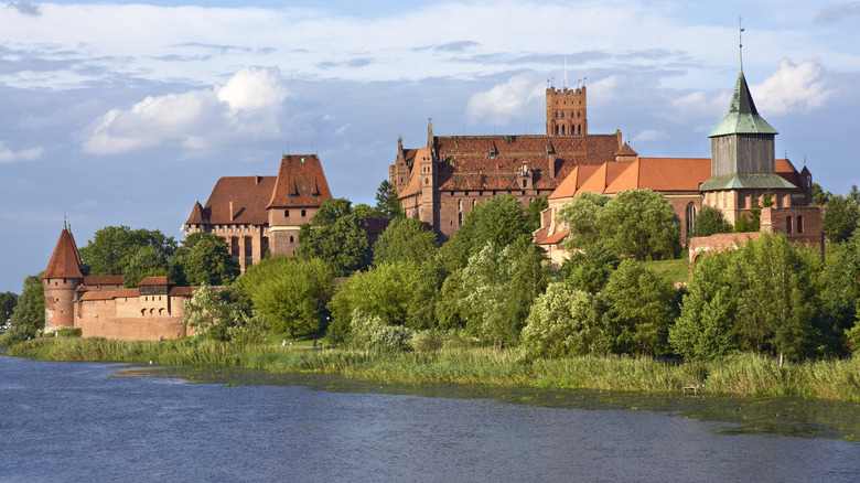 Towers and turrets of Malbork Castle along a grassy riverbank