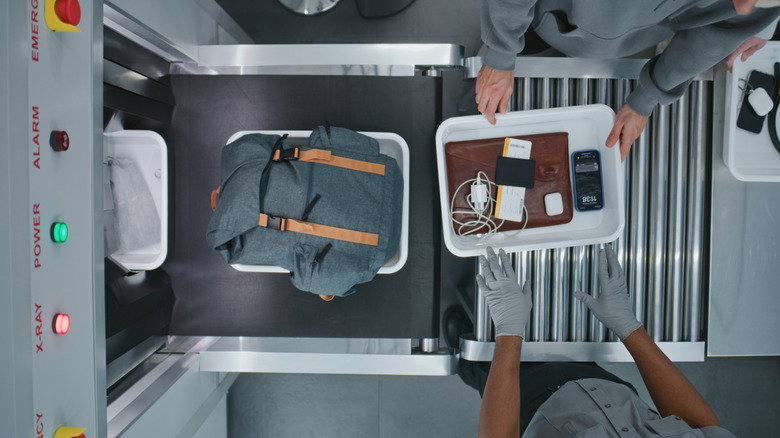Carry-on items are placed in trays on a conveyor belt at a security checkpoint in an airport