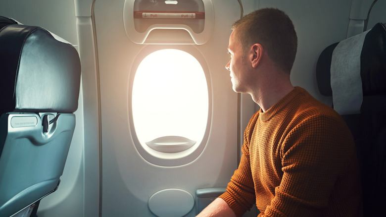 A man sits on an airplane with no belongings, looking out the window