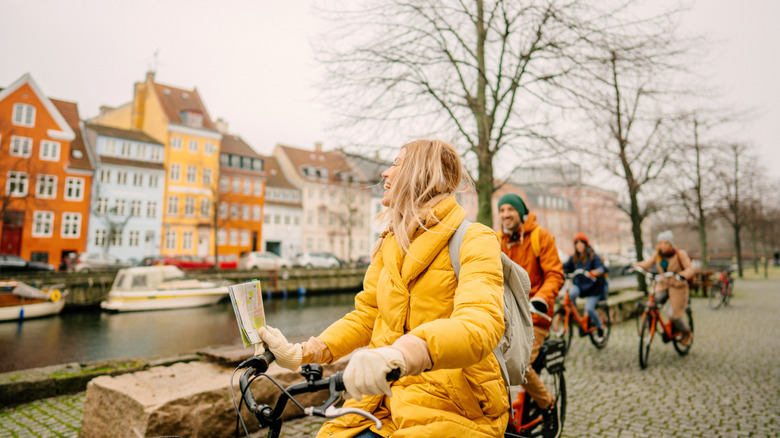 Blonde woman in a yellow coat leads a group of bikers along a canal in Copenhagen, Denmark