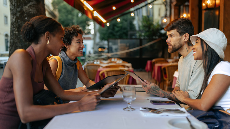 Group of young tourists reading menu and chatting at restaurant table in Rome