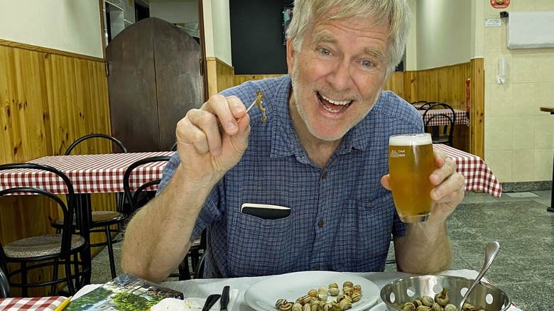 Rick Steves holding a small beer and eating a plate of snails in a Portuguese restaurant