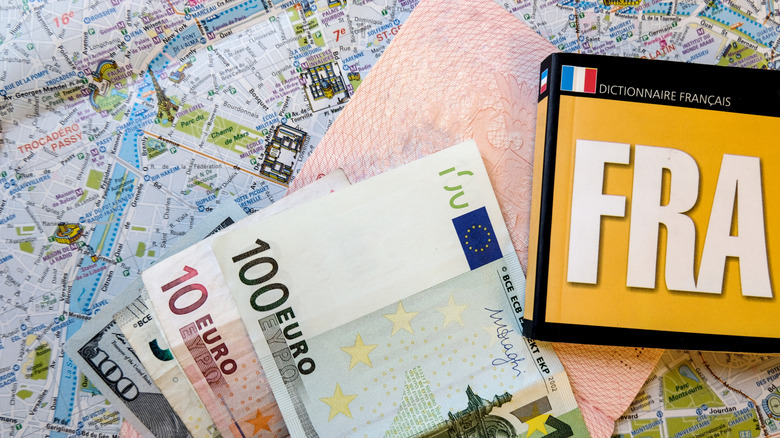 Close-up of travel accessories flat-lay, including passport, money, map, and French phrasebook