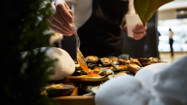 Close-up of a waiter's hand spooning sauce on mussels in a European restaurant