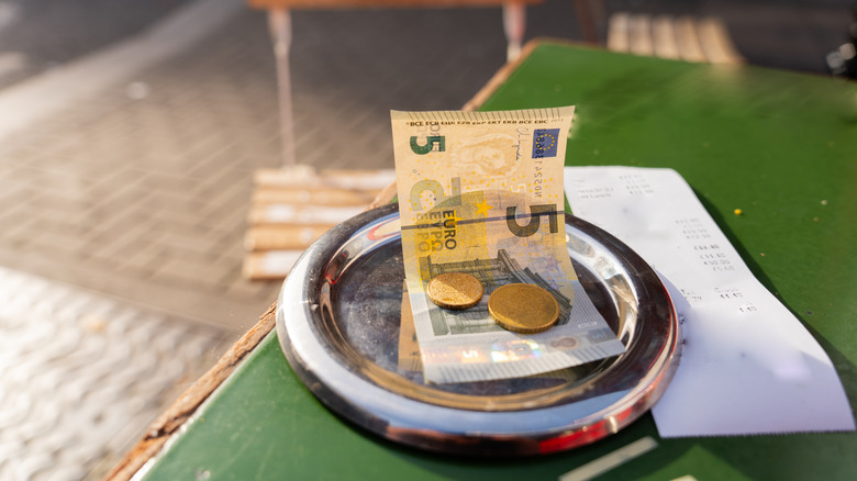 Close-up of a five Euro bill and coins on a table next to a receipt