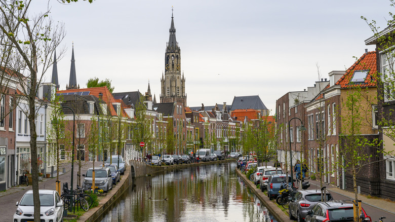 A canal lined with cars on a cloudy day in Delft