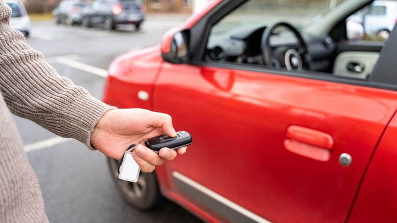 Hand holding a key fob towards a red car