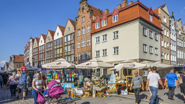 A city square in Gdansk, Poland, during the St. Dominic's Fair, with pedestrians and vendors under umbrellas