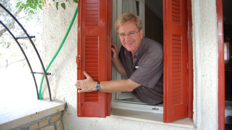 Rick Steves looking out a window with shutters