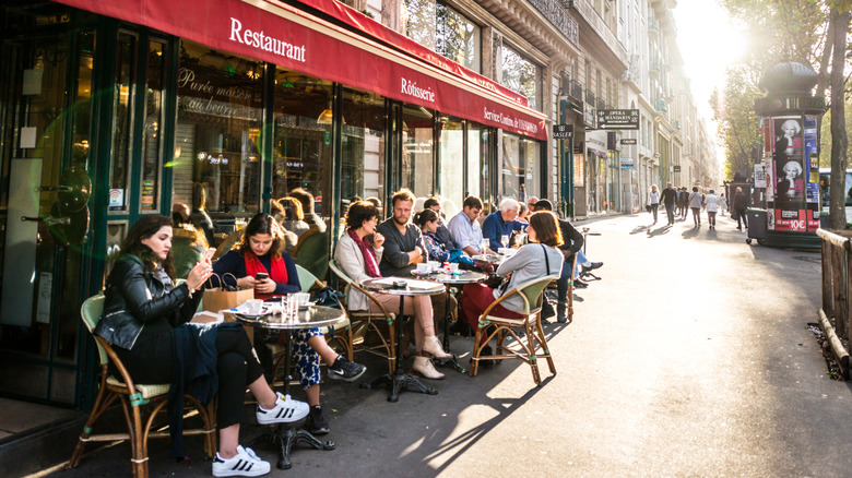 People sitting and eating at tables outside a restaurant in Paris, France