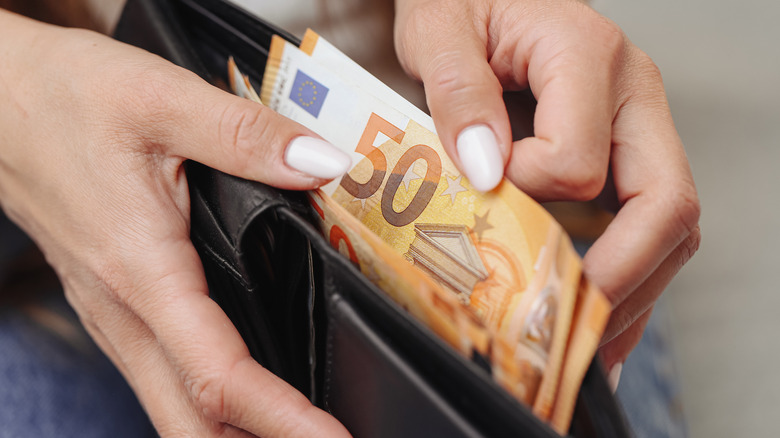 Someone pulling 50 euro bills out of a black wallet