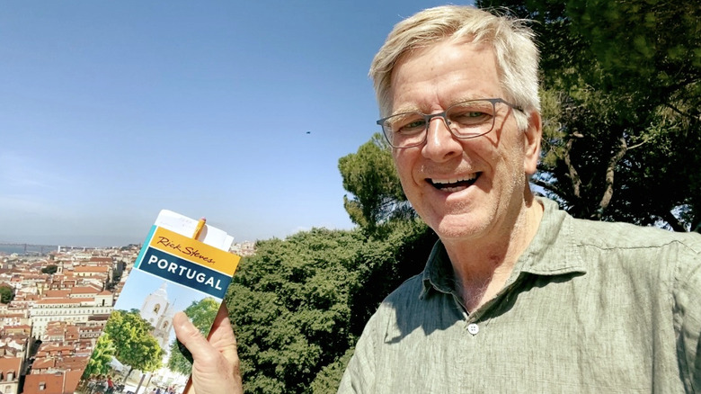 Travel author and TV personality Rick Steves poses with Portugal guidebook at scenic viewpoint.