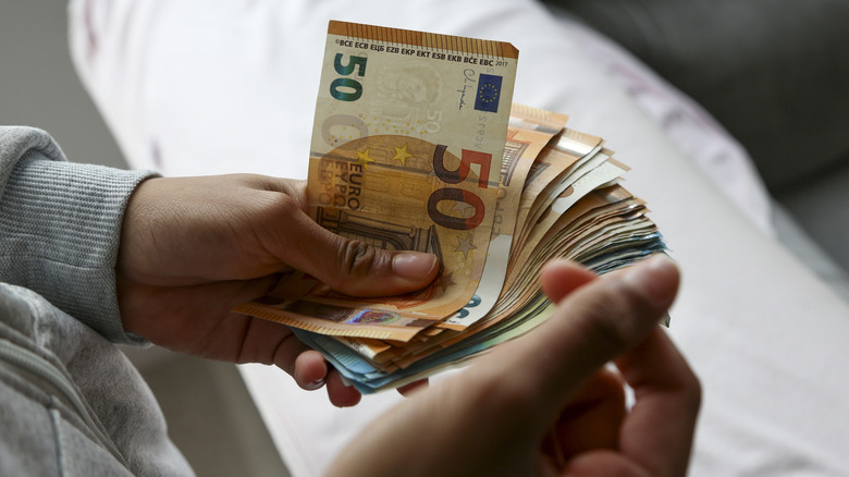 A wad of 50 euro bills held in a person's hands.