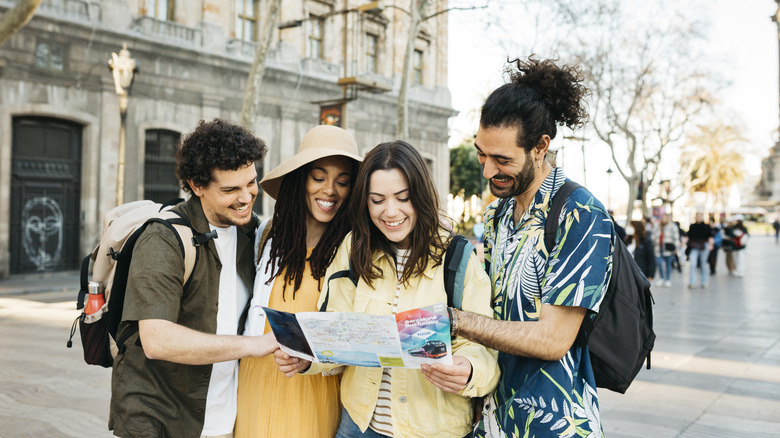 Four smiling friends consulting a map while visiting a European city