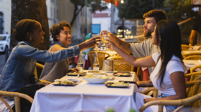 Four joyful friends are toasting drinks while sitting at a table, enjoying a meal together at an outdoor restaurant in lisbon, portugal, during the evening