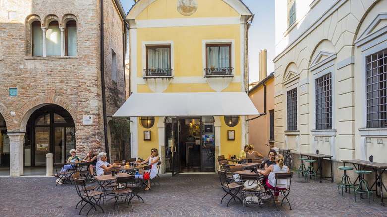 A charming yellow building with a small cafe inside and a terrace with people seated at tables.