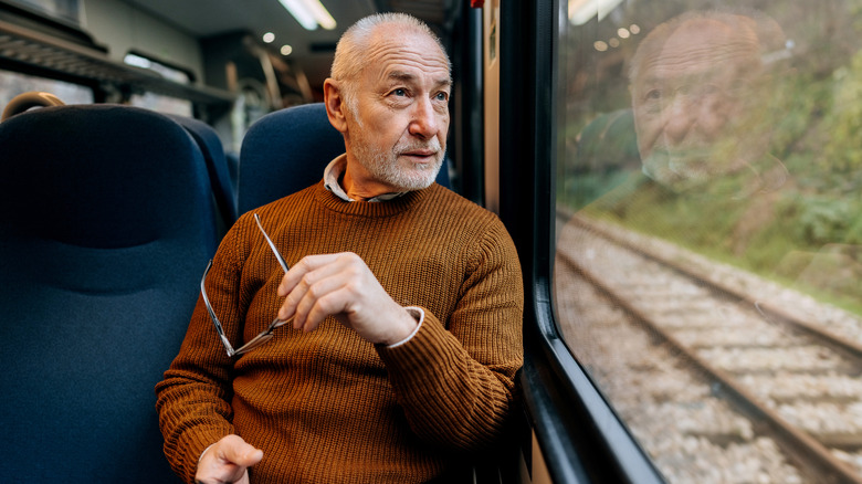An older man enjoying a view out the window while riding a train