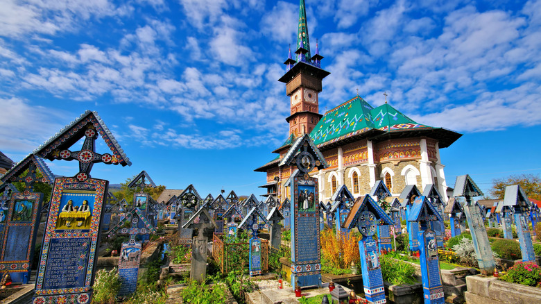 The Merry Cemetery in Romania with blue ornate wooden head stones and a colorfully roofed church