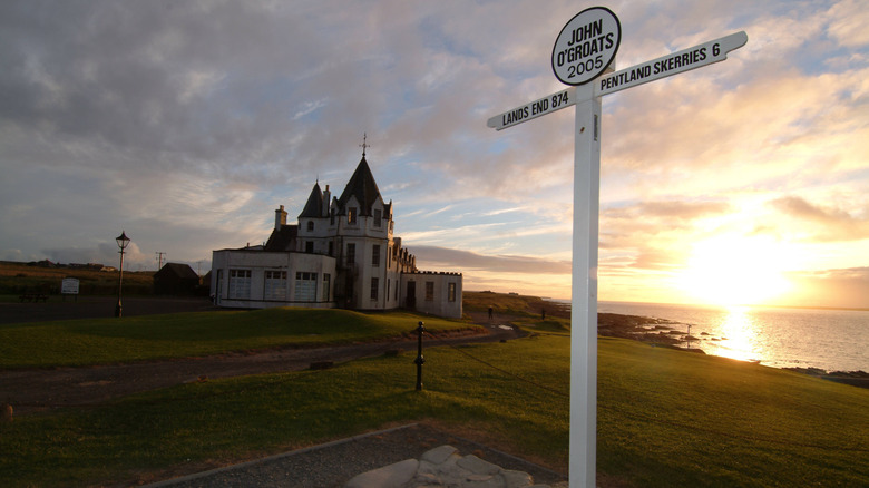 John O'Groats sign on the northern tip of the Scottish coast with historic inn in the background during sunset