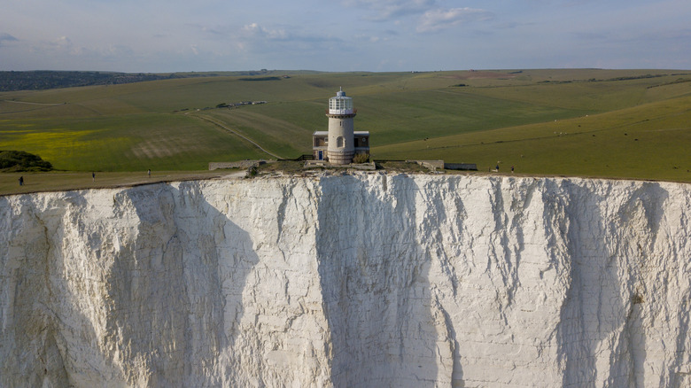 Lighthouse perched on the edge of the grass overlooking the white chalk Seven Sisters cliffs in England