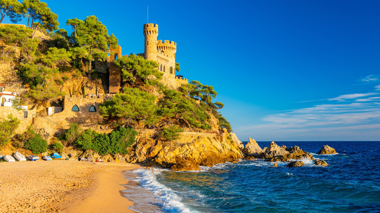 A red stone castle along the rocky, sandy coast near blue water in Costa Brava, Spain