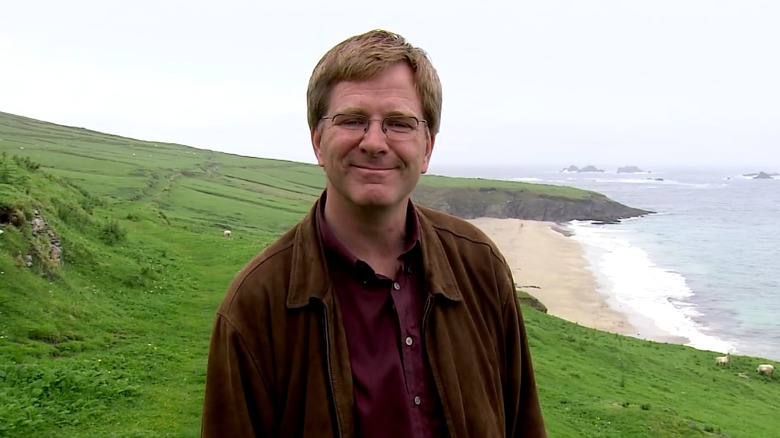 Rick Steves smiling on Blasket Island, with a view of the shore and grassy cliffs behind him