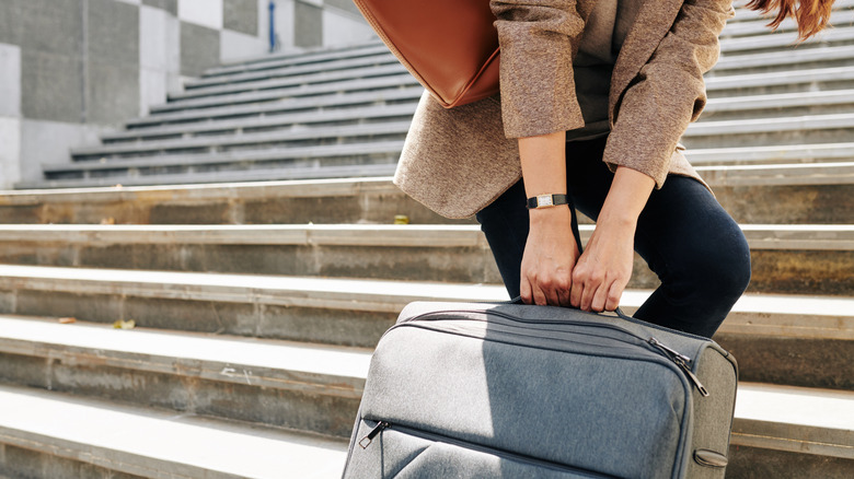 Traveler dragging a heavy suitcase up some stairs