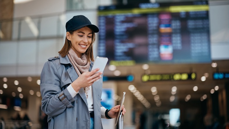 A happy woman walking through an airport while looking at her phone