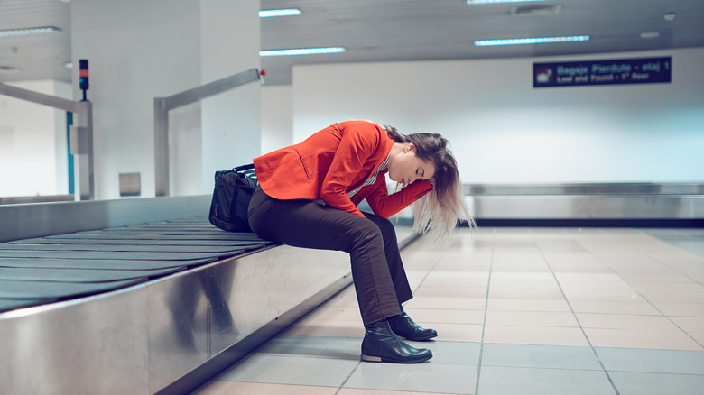 Woman inside the airport sitting on conveyor belt, loosing her suitcase, being frustrated.