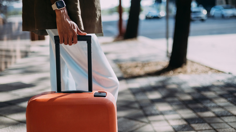 Close-up of a person holding an orange suitcase while walking on a city street during daytime.