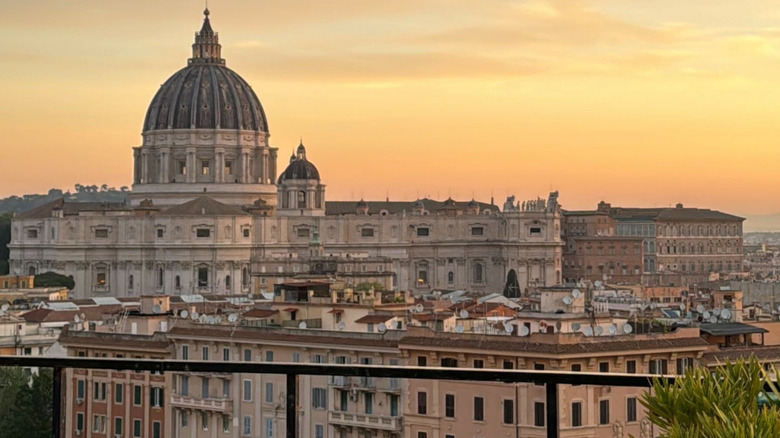 View of St. Peter's Basilica rising above the Roman skyline at sunset with a beautiful orange sky