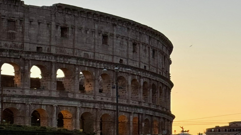 Close-up of the Roman Colosseum at sunset, with the structure almost silhouetted against an orange sky