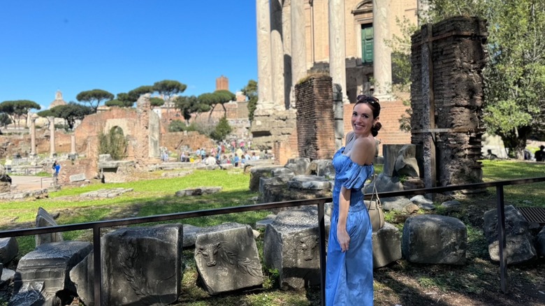 Brunette woman wearing a blue dress posing in the Roman Forum on a sunny day with ruins in the background