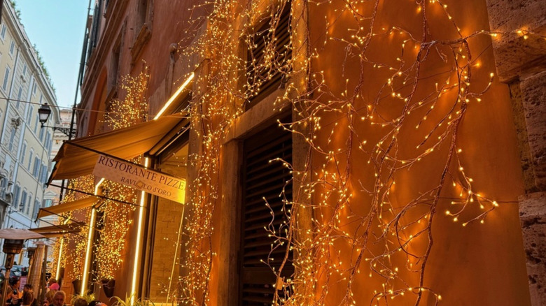 Fairy lights on a building in Rome's Trastevere neighborhood at dusk, with diners sitting at cafes