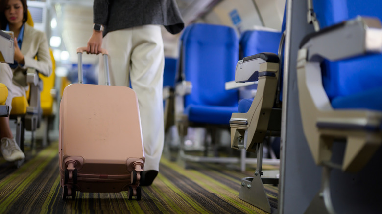 A woman pulling a small rolling suitcase between rows of seats