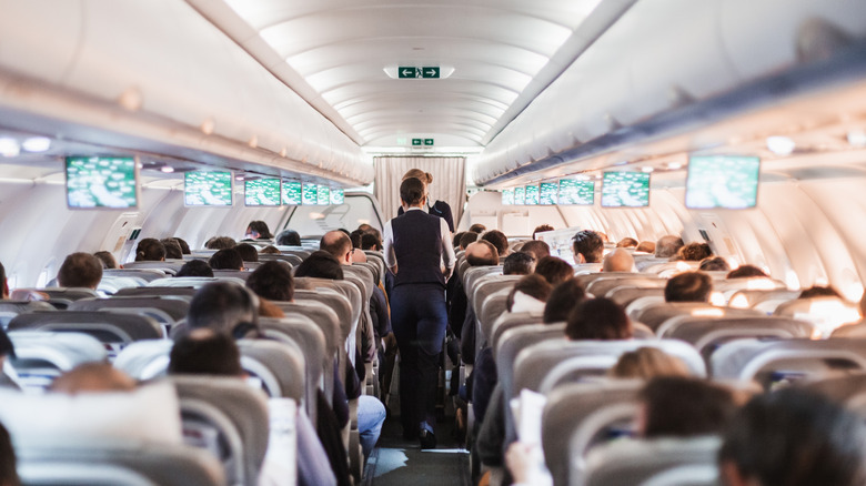 Rows of plane seats with passengers and flight attendants in the aisle