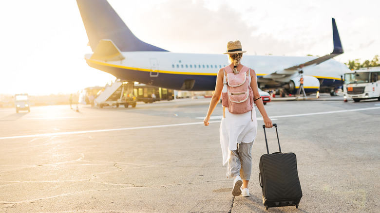 A woman pulling a suitcase while walking toward a plane