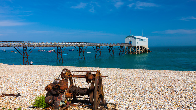A pier stretching out into the water on a beach with boats in the background