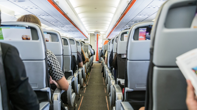 Passengers seated in an airplane cabin, viewed from the rear