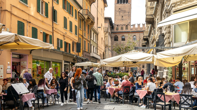 A Bologna street with pedestrians walking and dining under umbrellas