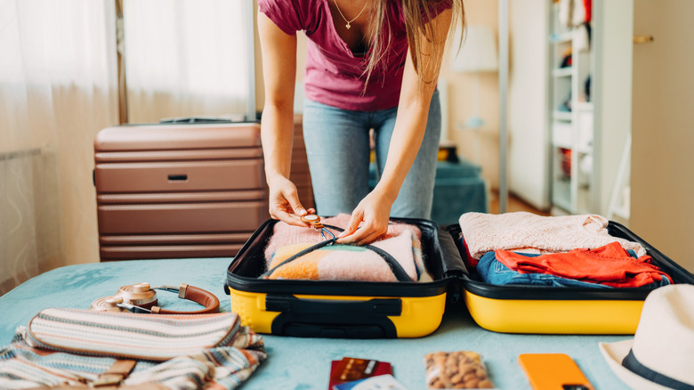 Someone packing a carry-on bag on a bed